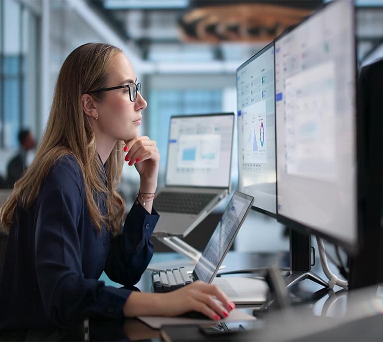 Business professional analysing operational data and workflow dashboards across multiple screens to manage business processes.