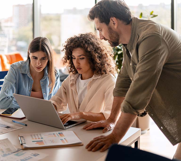 Business team reviewing technology plans, digital transformation initiatives and strategic investment opportunities using a laptop and planning documents.